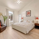 Bright-and-cozy-bedroom-with-white-upholstered-bed-frame-tufted-bedding-wooden-nightstands-with-red-lamps-and-brown-leather-armchair