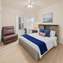 Rustic-gray-wooden-bed-frame-with-barn-door-headboard-white-and-blue-bedding-and-brown-leather-accent-chair